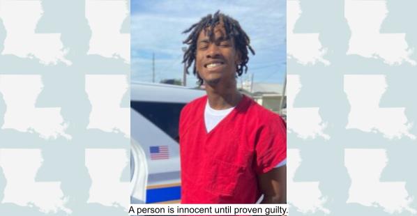 A 20 year old black male wearing a bright orange or red short-sleeve V-neck shirt with a white under shirt. The man appears to be wearing handcuffs in Louisiana.