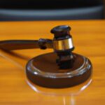 A judges gavel on a highly polished light brown wood table with a black leather chair in the background.