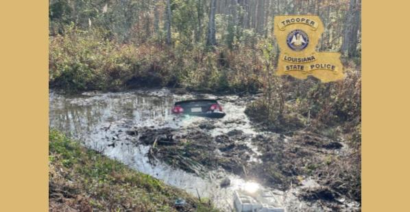 A black passenger car almost completely submerged in a wet muddy area.